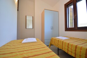 Una habitación con dos camas individuales, un armario, un espejo y una ventana con persianas.