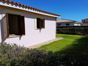 Uma casa térrea com telhado de telhas, um pequeno jardim frontal e um viveiro.