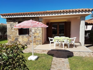 Un edificio de piedra con techo de tejas, un patio con mesa y sillas, y una sombrilla a rayas.