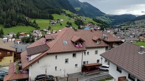 A mountain town with traditional architecture, a prominent hotel with a sign, and a view of the surrounding hills and green valleys. - Hotel Pension Sonnalp (Ortisei)
