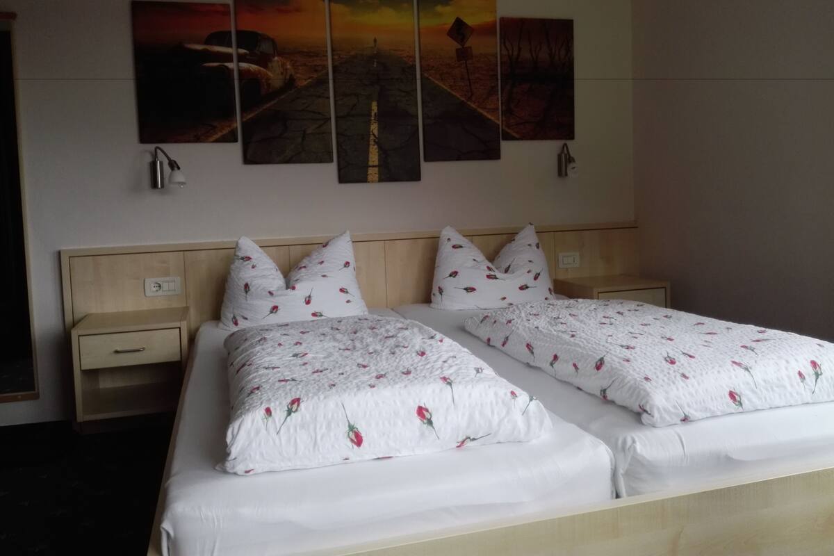 Un lit double avec une literie à motifs floraux, une tête de lit en bois et une table de chevet avec une lampe.