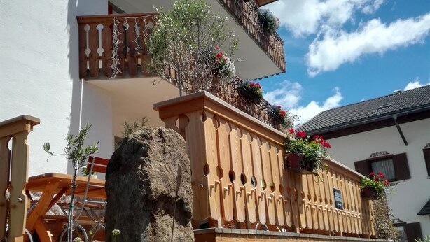 A building with wooden balconies, a large rock, and a flower bed. - Hotel Pension Sonnalp (Ortisei)