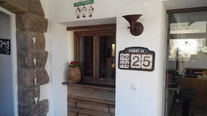 A stone wall with a rustic wooden door, a small vase with flowers, and a wall-mounted clock displaying the date. - Hotel Pension Sonnalp (Ortisei)