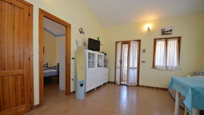 A room with a bed, a white cabinet, a table with a blue tablecloth, and a wooden door. - Casa Nadia (San Teodoro)