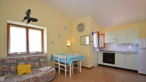 A living room with a sofa, a dining table, and a kitchen area with cabinets and a refrigerator. - Casa Nadia (San Teodoro)