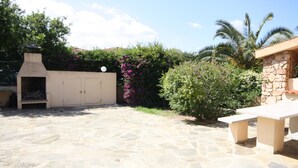 A stone patio with a barbecue area, a stone wall, and a small table. - Casa Nadia (San Teodoro)