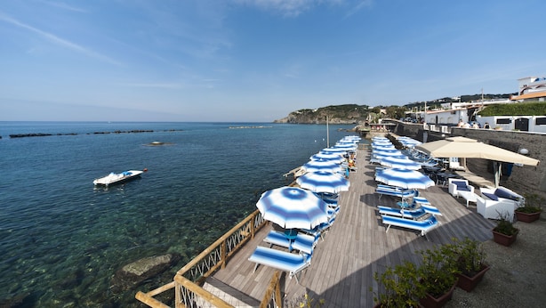 A pier with sun umbrellas and lounge chairs overlooking a clear blue sea.