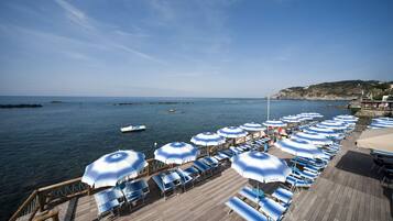 Une terrasse en bois, bordée de rangées de parasols bleus et blancs et de chaises longues, donnant sur une mer calme.