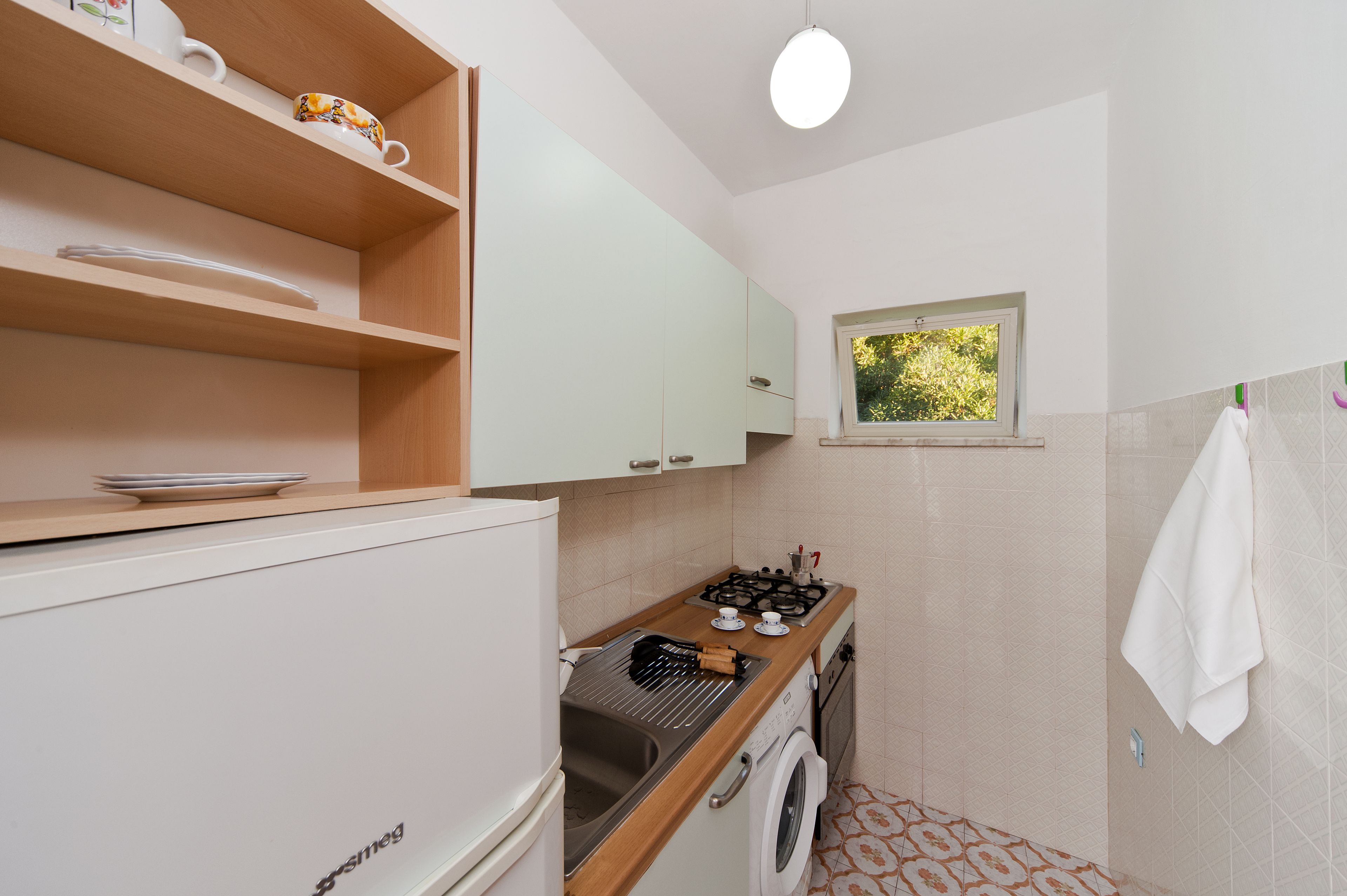 A compact kitchen with a washing machine, a small window, and a towel hanging on the wall.