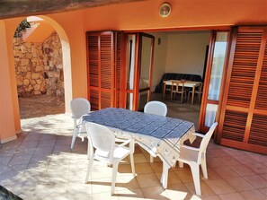 A patio with a table and chairs, a stone wall, and wooden shutters.