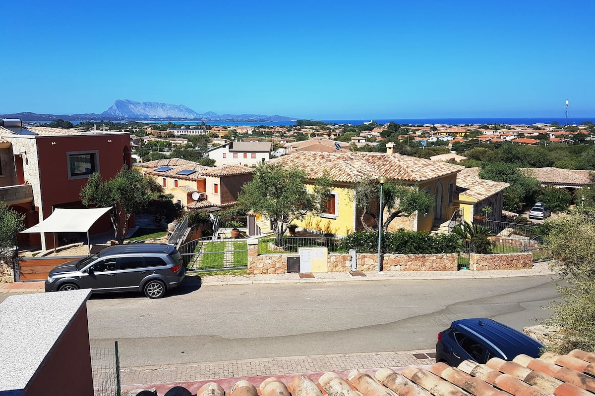 Uma área residencial costeira com casas de telhados em terracota e vista clara para o mar.