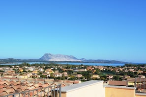 A coastal town with terracotta-roofed buildings, a mountain in the background, and a clear blue sky. - Citai Apartment (San Teodoro)