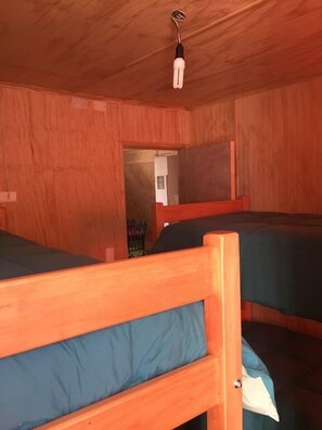 A room with wooden bunk beds, a ceiling light, and a door leading to another room.