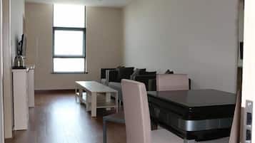A modern, minimalist living room with a sofa set, a dining table, and a kitchen area with a kettle.