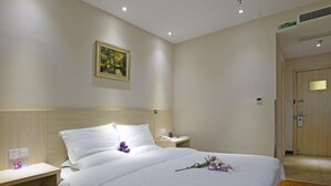 A hotel room with a neatly made bed, a bedside table with a lamp, a wall-mounted painting, and a door in the background. - GreenTree Alliance Suzhou Zhangjiagang Huachang Road Bus Station Hotel (Suzhou)