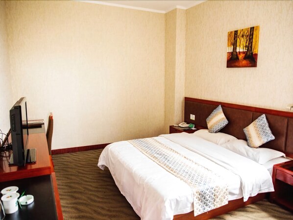 A hotel room with a bed, a desk with a computer, a telephone, and a painting on the wall.