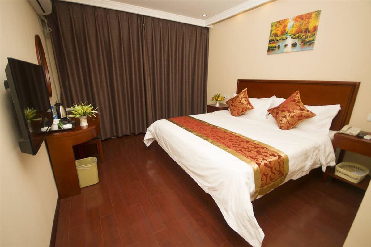 A hotel room with a large bed, a TV, a desk, and a window with curtains.