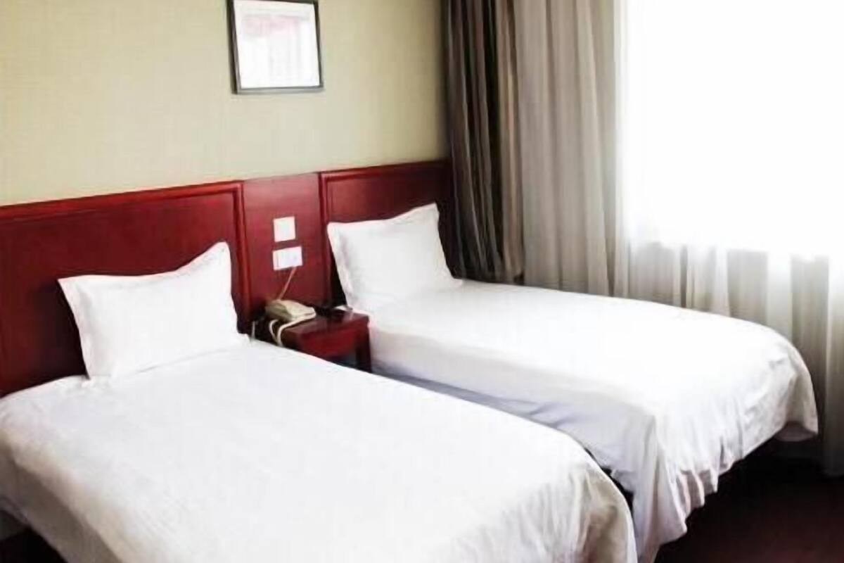 A hotel room with two single beds, a red headboard, a bedside table with a phone, and a window with curtains.