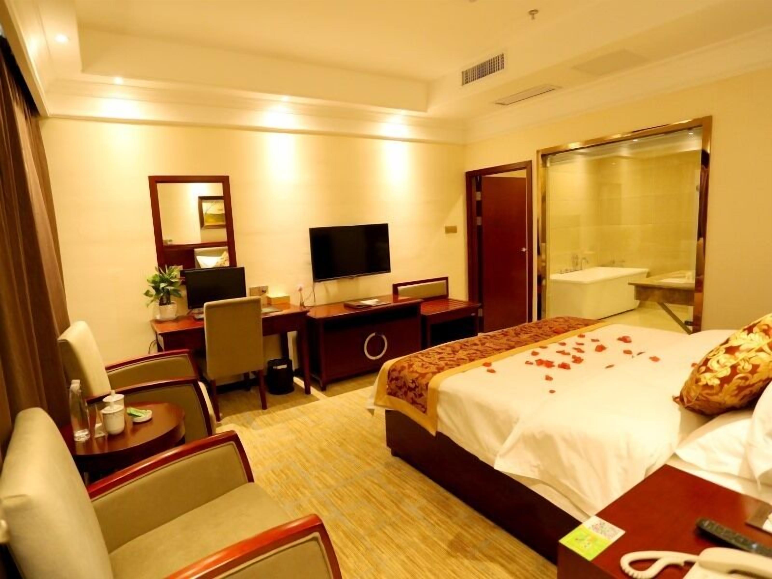 Une chambre d’hôtel comprenant un lit, un bureau avec un ordinateur, une télévision, une chaise, une petite table avec un téléphone, et une salle de bain avec une baignoire et un miroir.