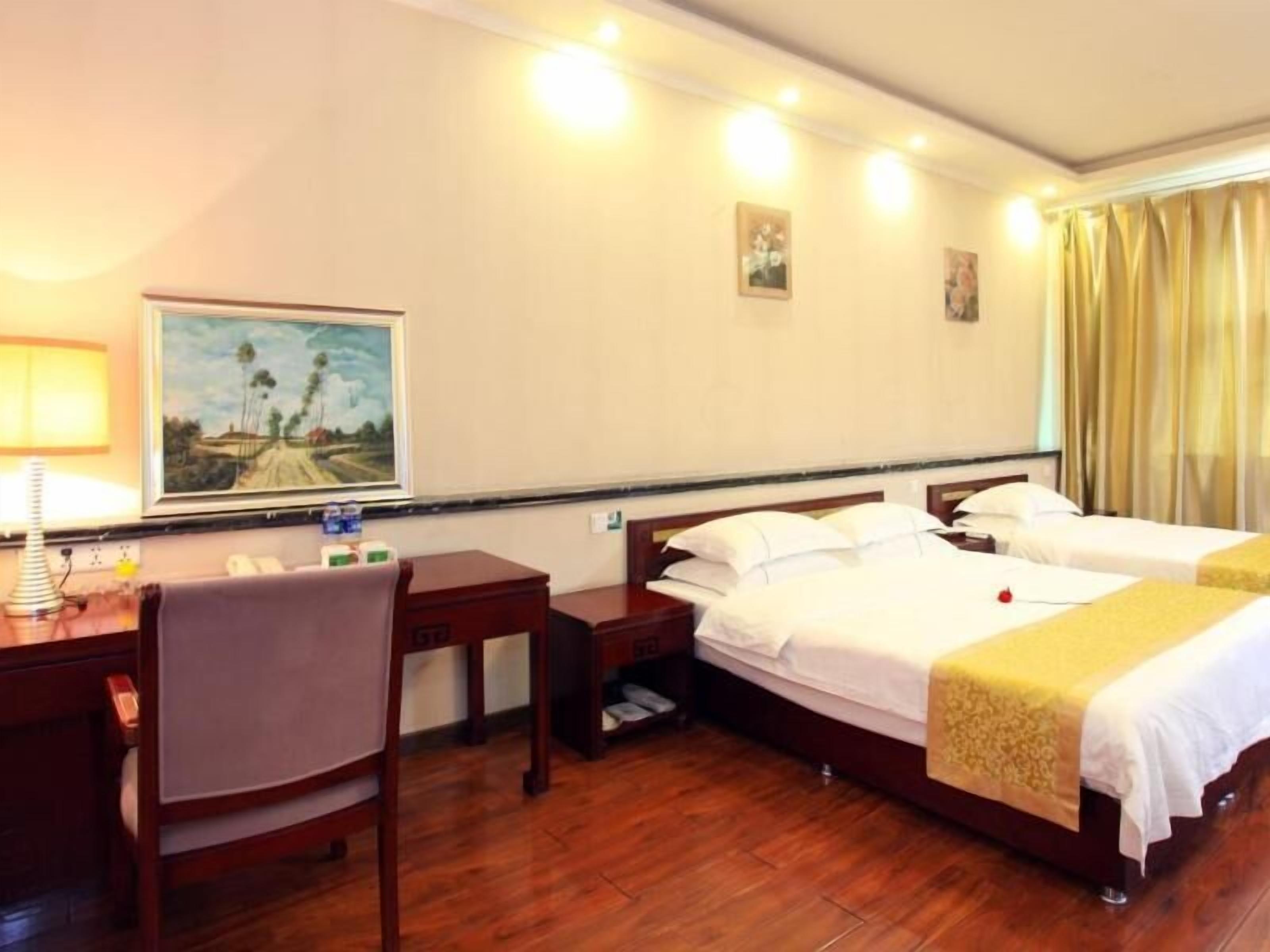 A hotel room with two beds, a desk, a chair, and a painting on the wall.