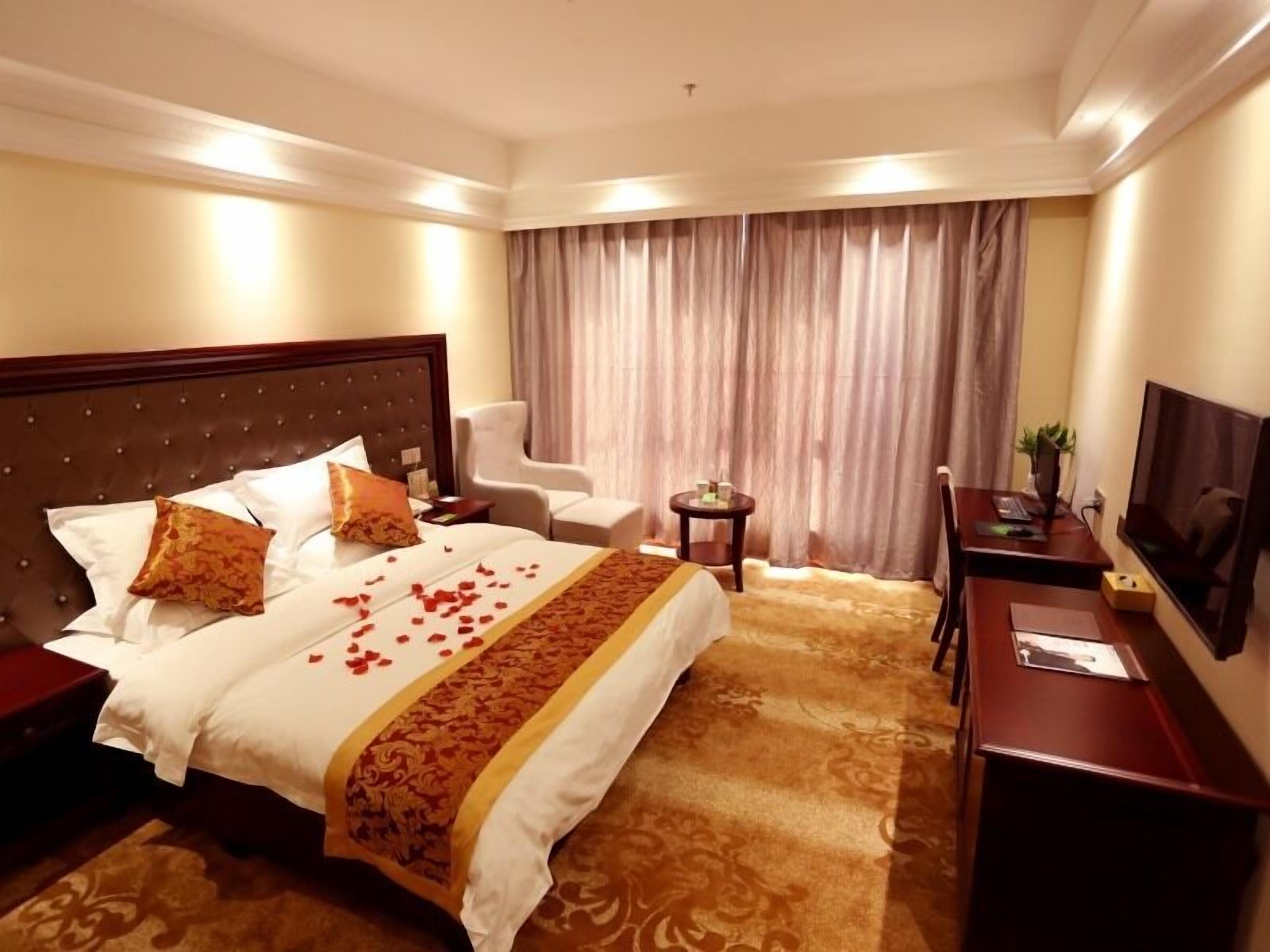 Habitación de hotel con una cama grande, un escritorio, una silla, un televisor y una ventana con cortinas.