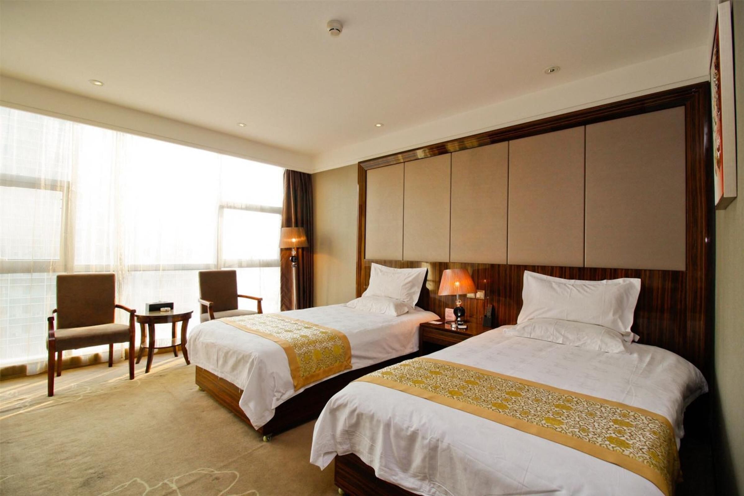 A hotel room with two beds, a large window with curtains, a desk, and a chair.