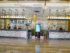 Un espace d’accueil d’hôtel comprenant deux comptoirs de réception, du personnel et un panneau d’affichage numérique.
