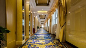 A hotel corridor with a blue and yellow patterned carpet, yellow walls, and a ceiling with floral design.