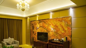 A modern living room with a large flat-screen TV, a chandelier, and a wall with a nature-inspired mural.