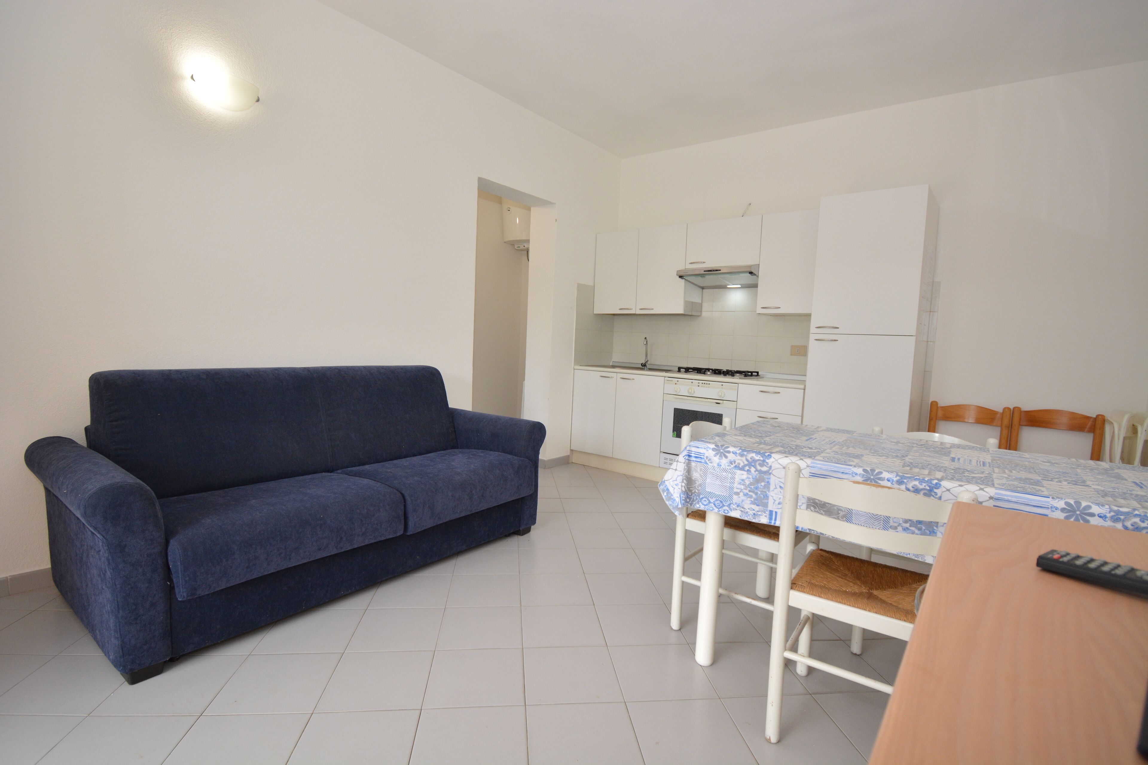 A compact living space with a sofa, a dining table with a patterned tablecloth, and a kitchenette in the background.