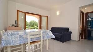A dining area with a table covered in a blue and white patterned tablecloth, a blue sofa, and a kitchen visible through an open door. - Coclearia Apartment (San Teodoro)