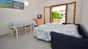 A bedroom with a bed, a desk with a chair, a television, and a balcony with a view of the outside. - Coclearia Apartment (San Teodoro)