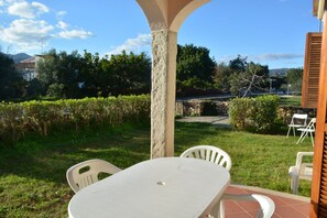 Un patio con mesa y sillas, rodeado de follaje y un muro de piedra.