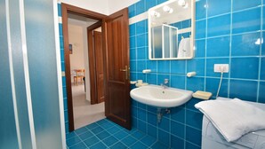 A bathroom with blue tiles, a white sink, a mirror, and a towel on a washing machine. - Coclearia Apartment (San Teodoro)