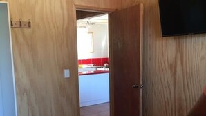 A room with wooden walls, a bed with blue bedding, and a TV mounted on the wall. - Cabaña en Algarrobo 4 El Canelo (Algarrobo)