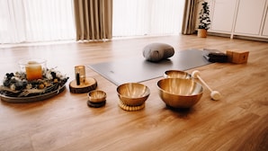 A room with a wooden floor, a yoga mat, a meditation cushion, and several bowls. - Okelmann's (Warpe)