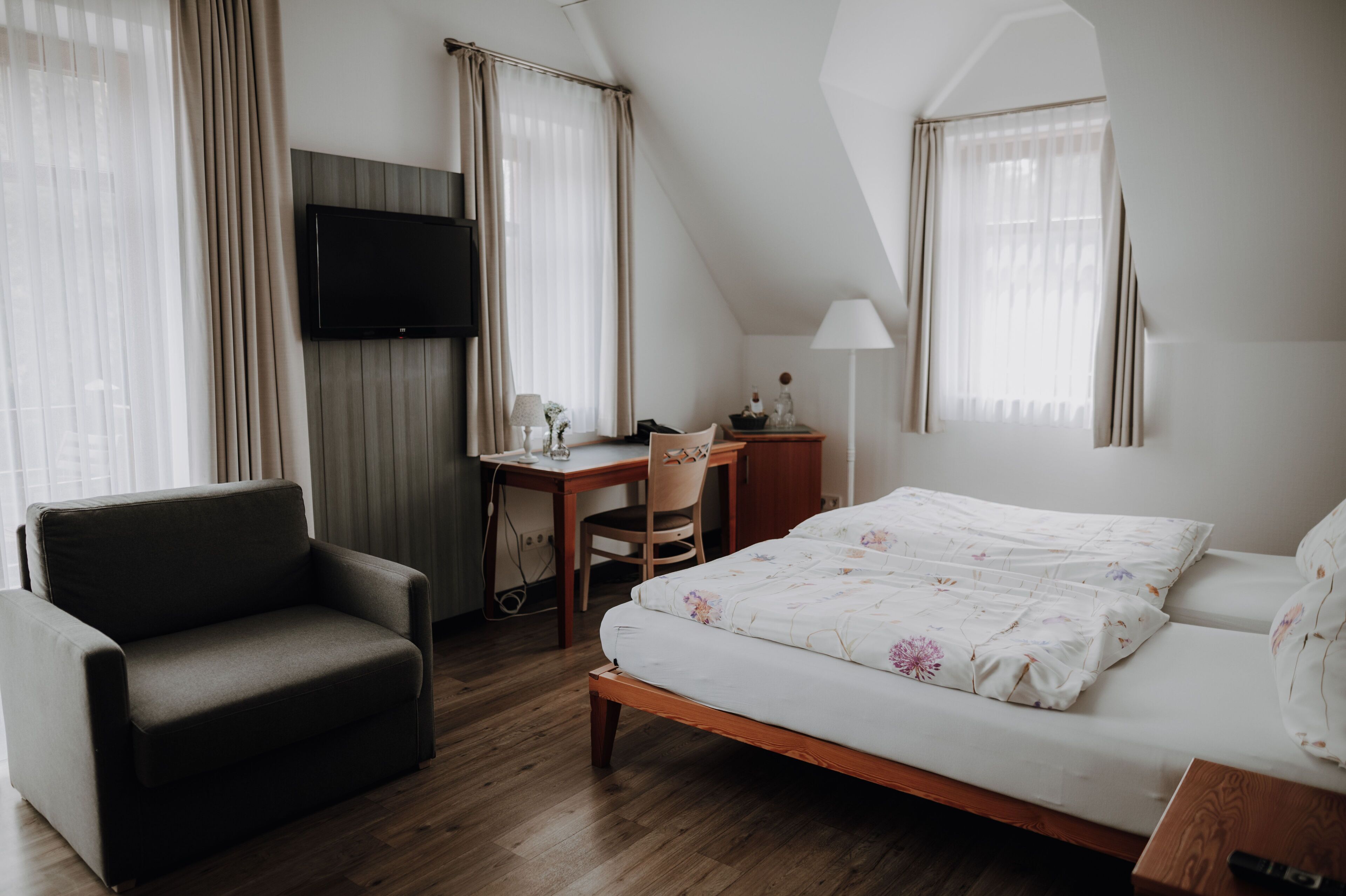 A bedroom with a bed, a desk, a chair, a TV, and curtains.
