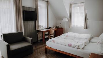 A bedroom with a bed, a desk, a chair, a TV, and curtains.