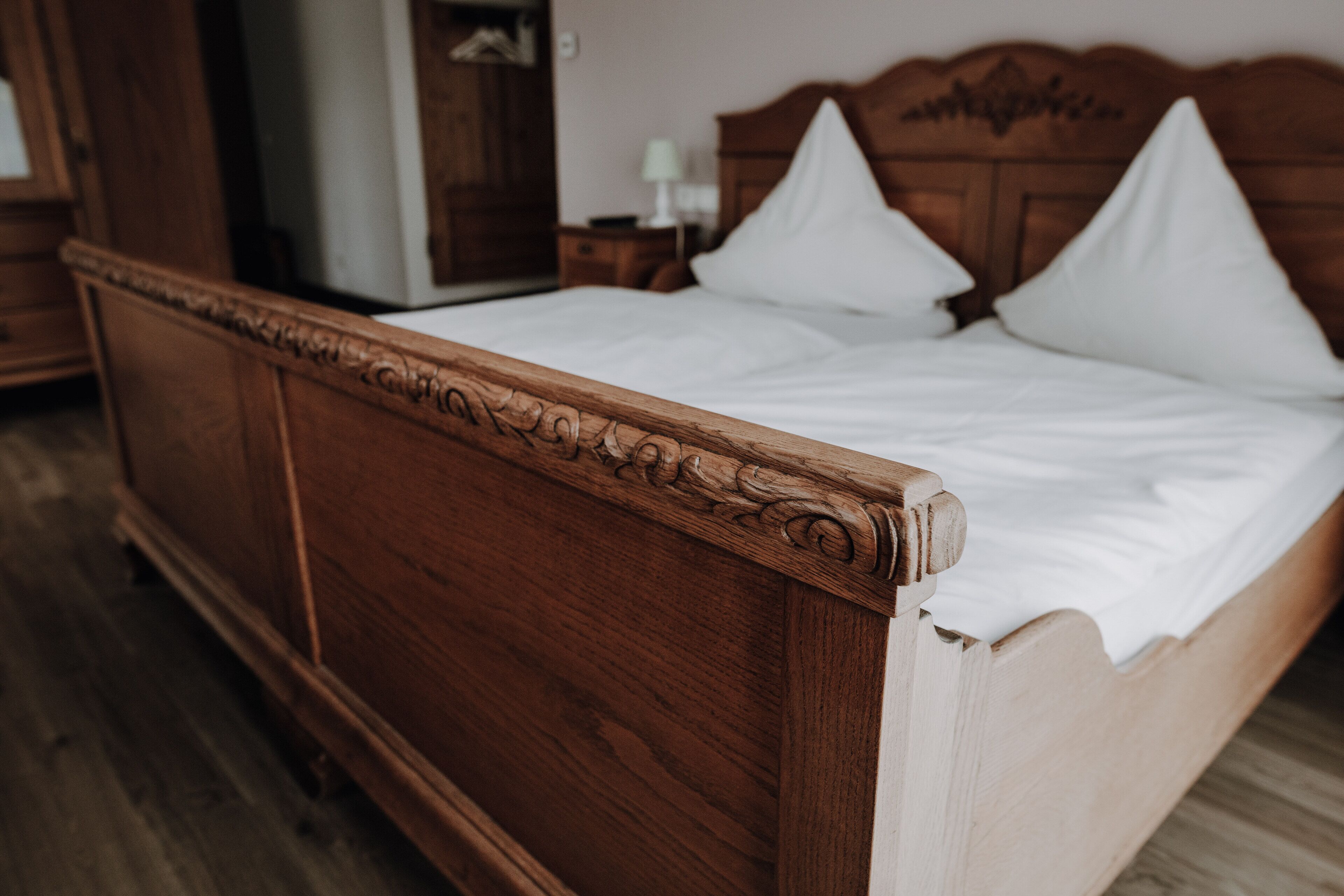 A wooden bed with a headboard, white bedding, and a wooden floor.