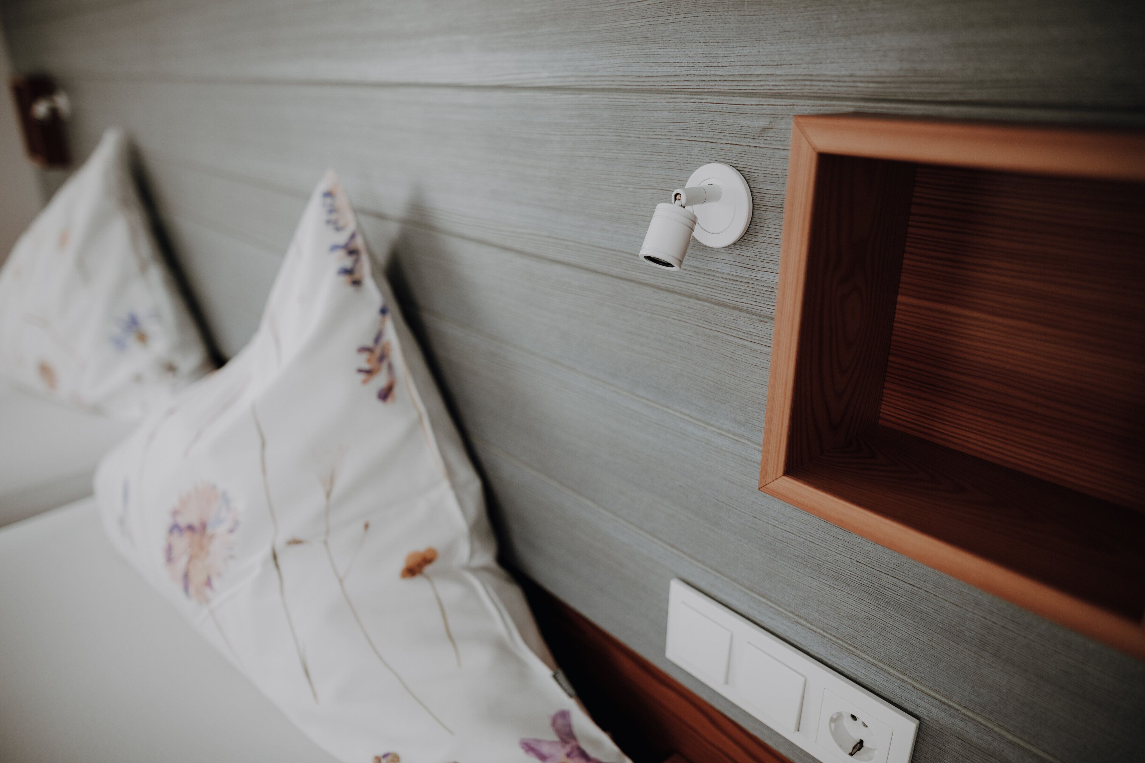 A bed with floral bedding, a bedside table, and a wall-mounted light fixture.