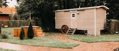 Una pequeña cabaña de madera con un porche de madera adjunto, rodeada por un patio cubierto de césped y un camino de ladrillo.