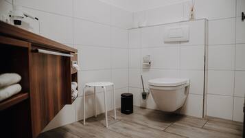 A bathroom with a wooden vanity, a toilet, a trash bin, and a small white stool.