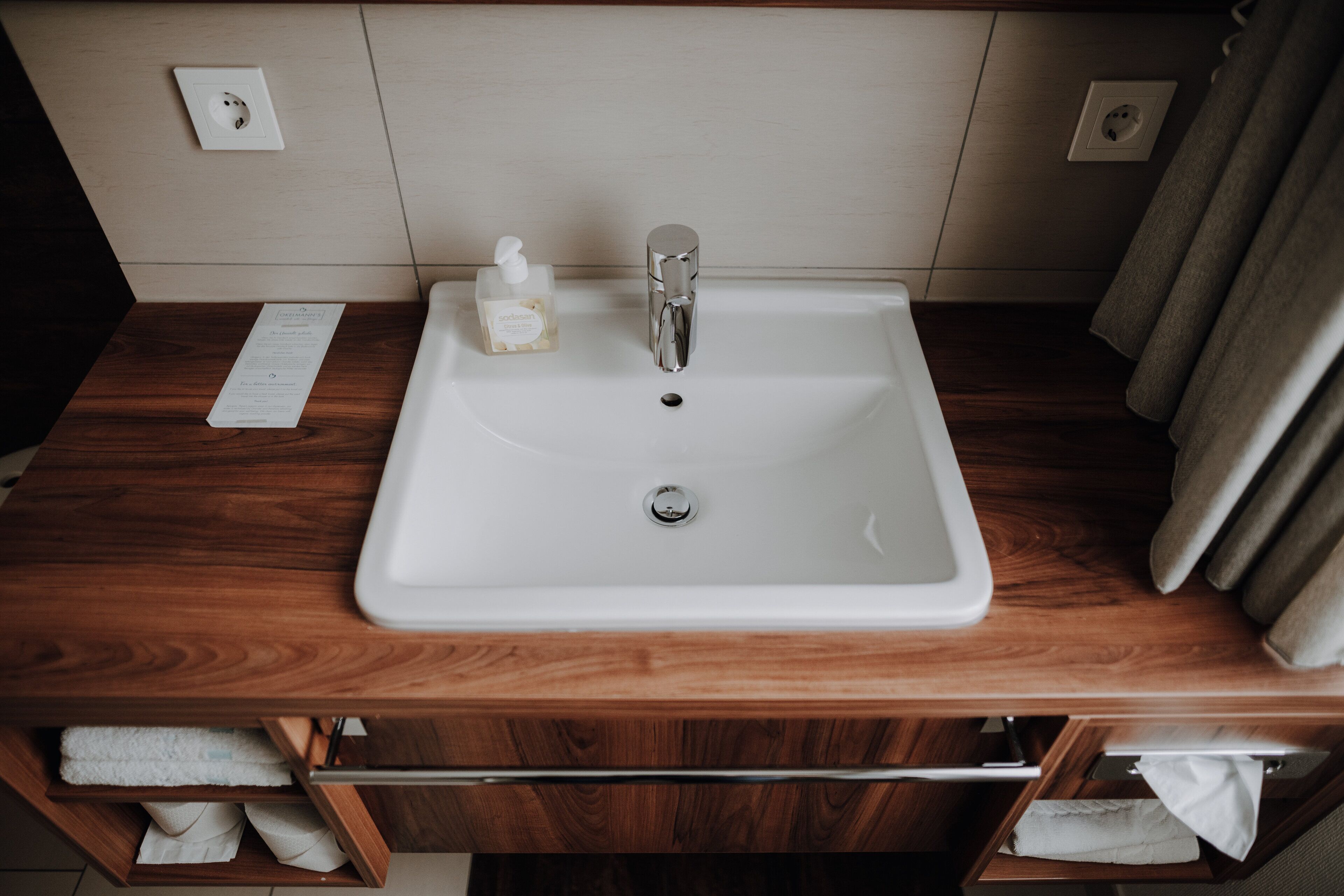 A bathroom with a wooden vanity, a white sink, and a bottle of hand soap.