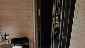 A modern bathroom with a glass-enclosed shower, wooden flooring, and a grey sofa. - Okelmann's (Warpe)