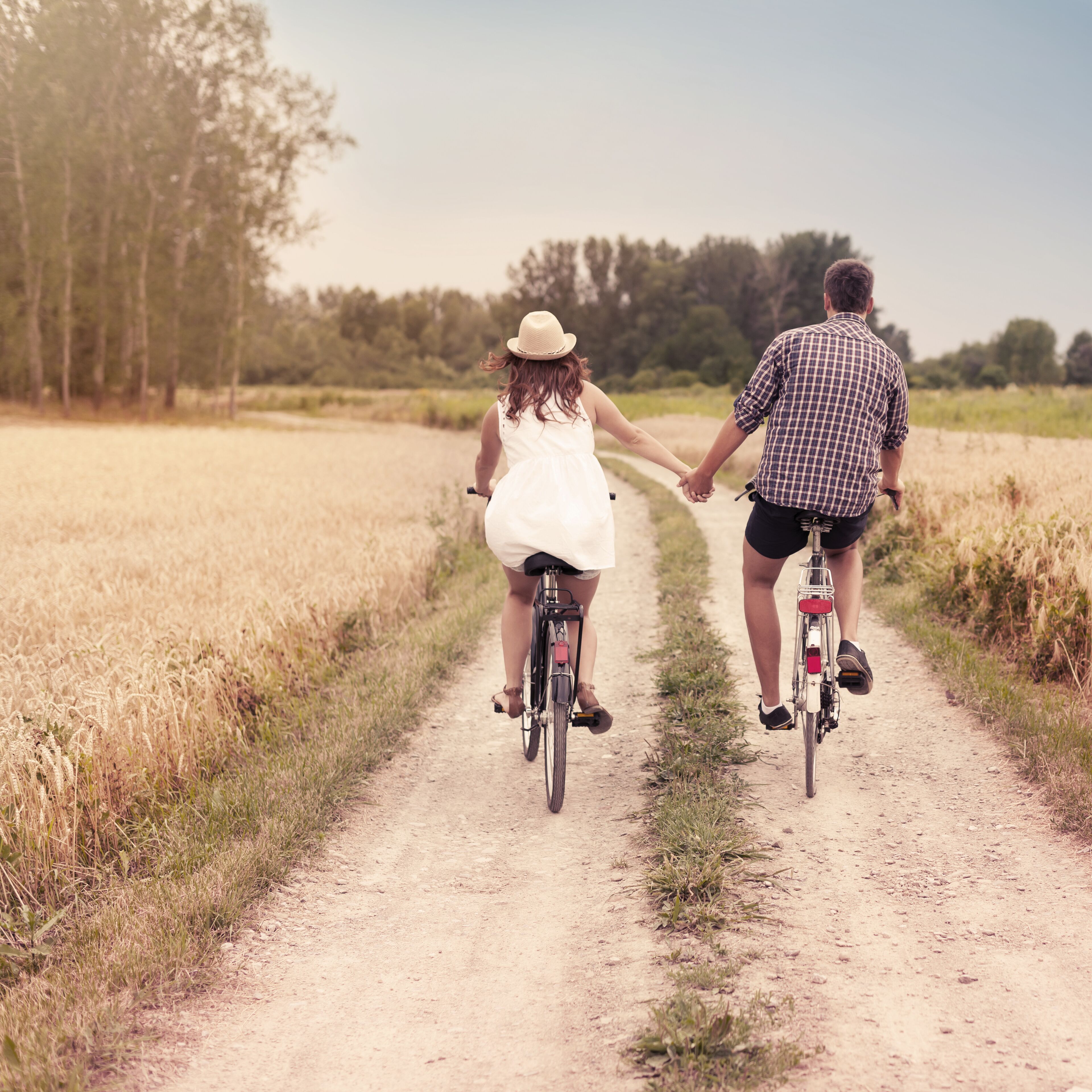 Two people on bicycles on a dirt path surrounded by fields.