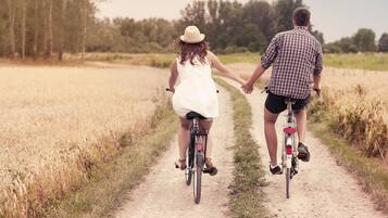 Two people on bicycles on a dirt path surrounded by fields.