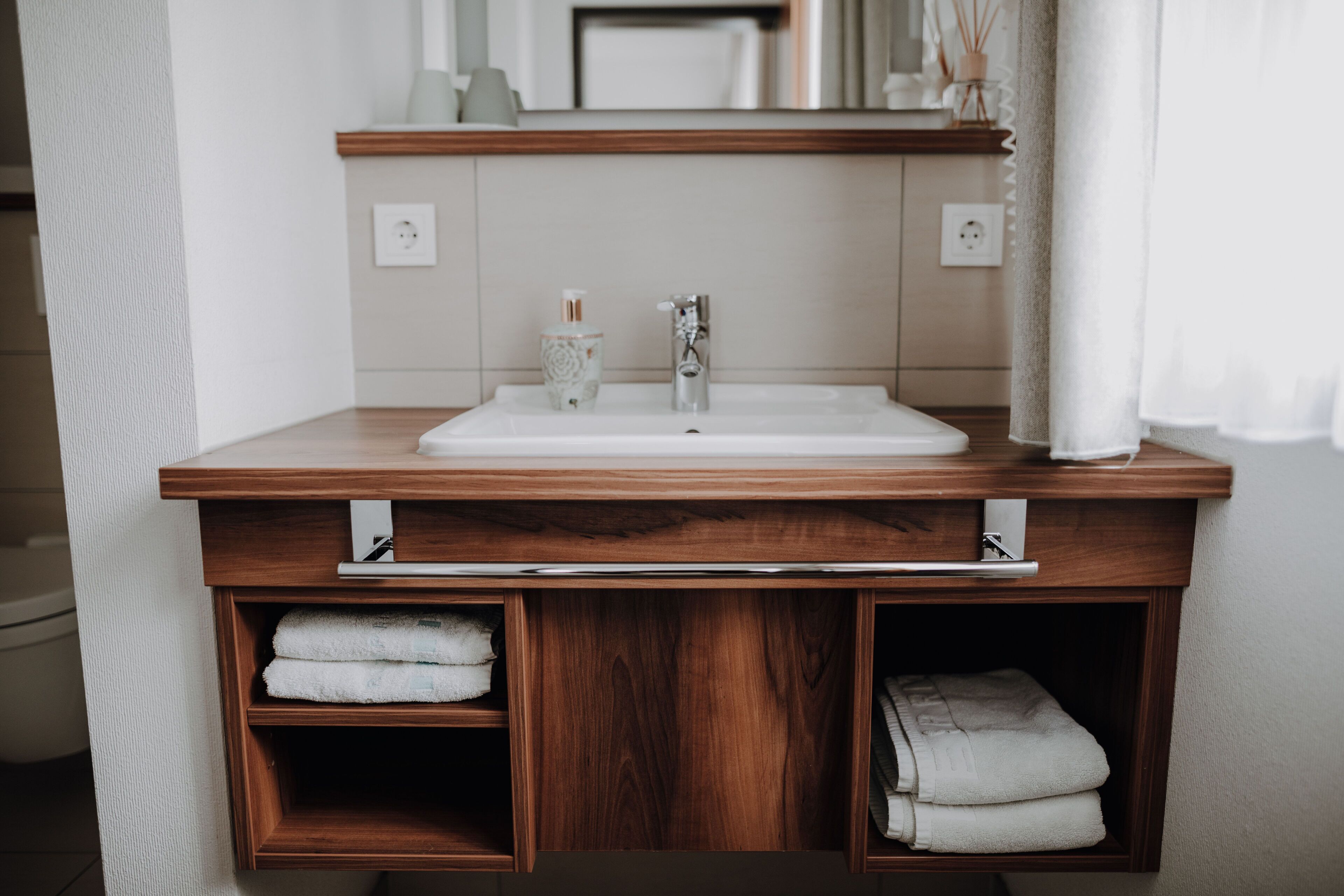 A bathroom with a wooden vanity, a white sink, and two towel shelves.