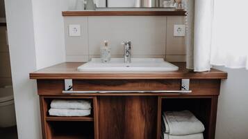 A bathroom with a wooden vanity, a white sink, and two towel shelves.