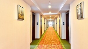 Un pasillo de hotel con suelo alfombrado, puertas a ambos lados y cuadros enmarcados en las paredes.