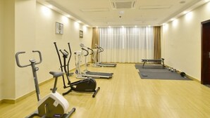 Un gimnasio con máquinas de cardio, una banca y colchonetas sobre piso de madera.